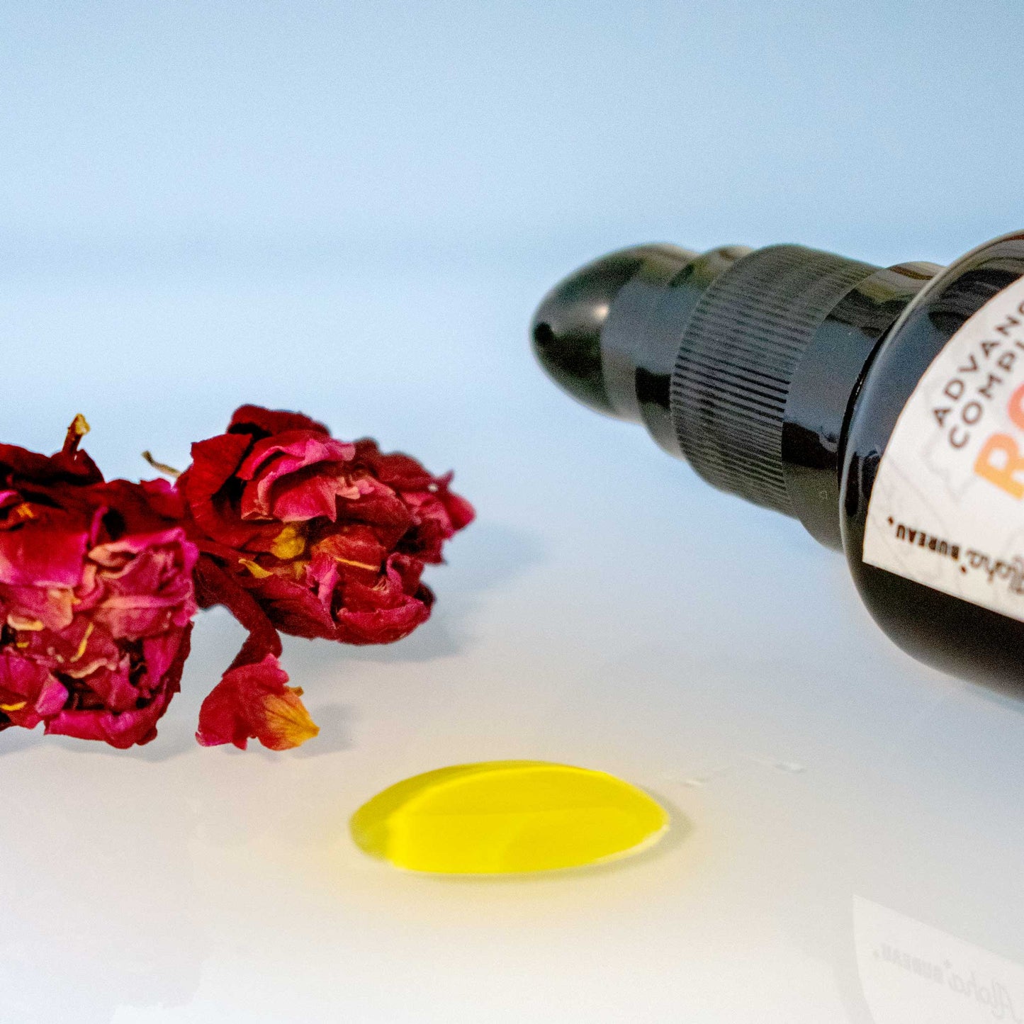 Close up detail of Rose Gold + Bakuchiol oil serum with bottle and dried roses.