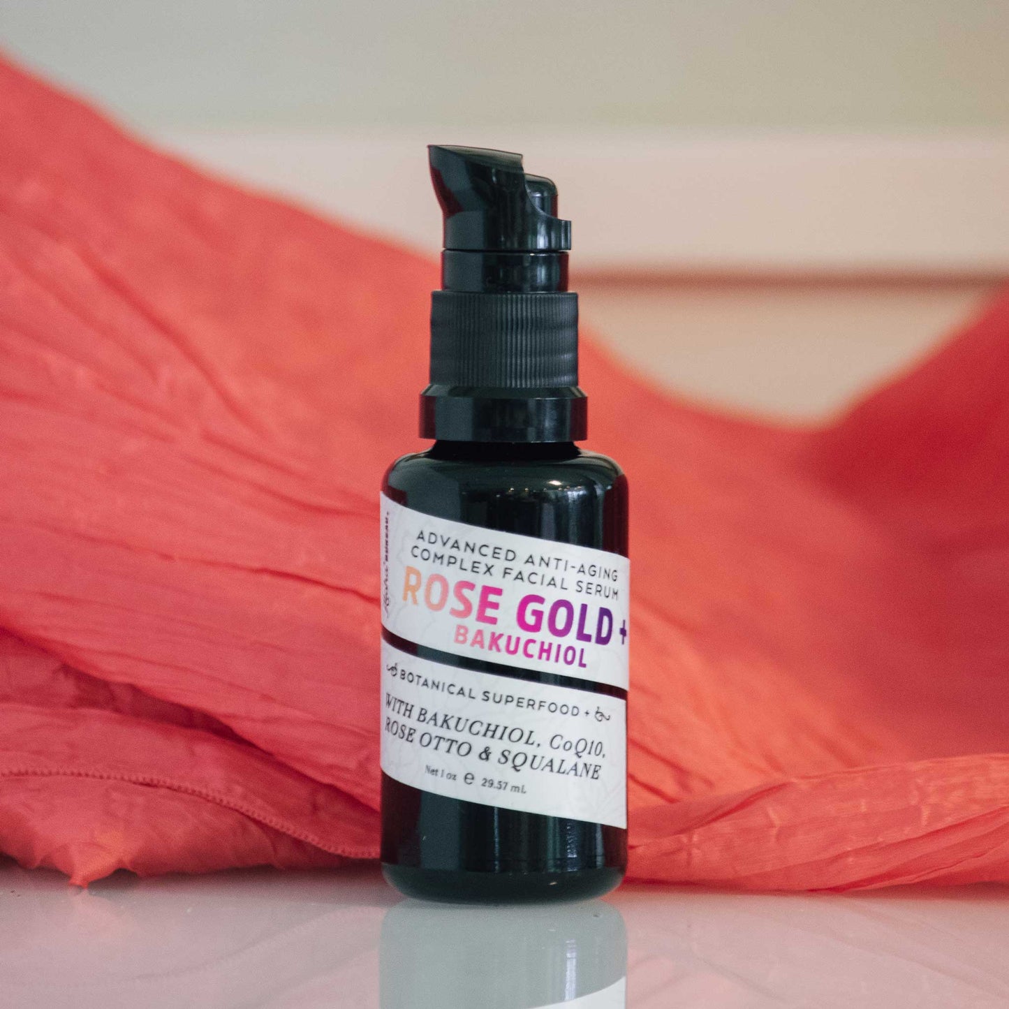Rose Gold + Bakuchiol 1oz serum bottle with a bright pink satin background
