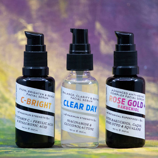 Three facial serum bottles labeled 'C-Bright', 'Clear Day', and 'Rose Gold+Bakuchiol' on a bright textured painted background